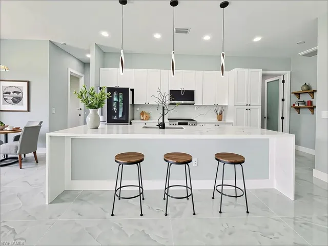 Kitchen featuring light marble finish flooring, black fridge, a spacious island, a kitchen breakfast bar, and white cabinets
