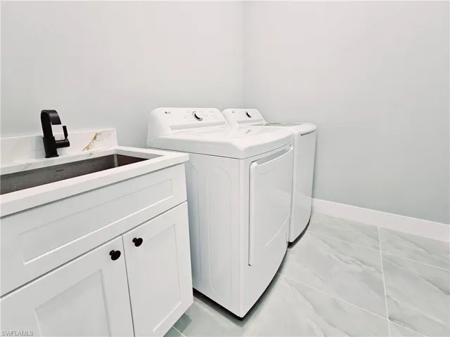 Laundry area with independent washer and dryer, cabinet space, and light marble finish floors