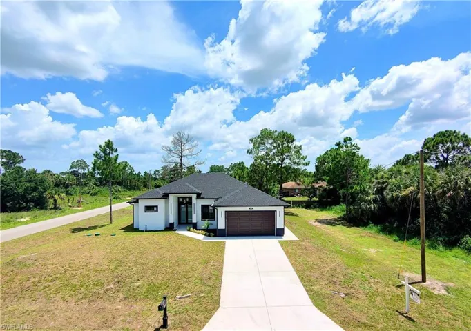 View of front of home with concrete driveway, an attached garage, a front yard, stucco siding, and roof with shingles