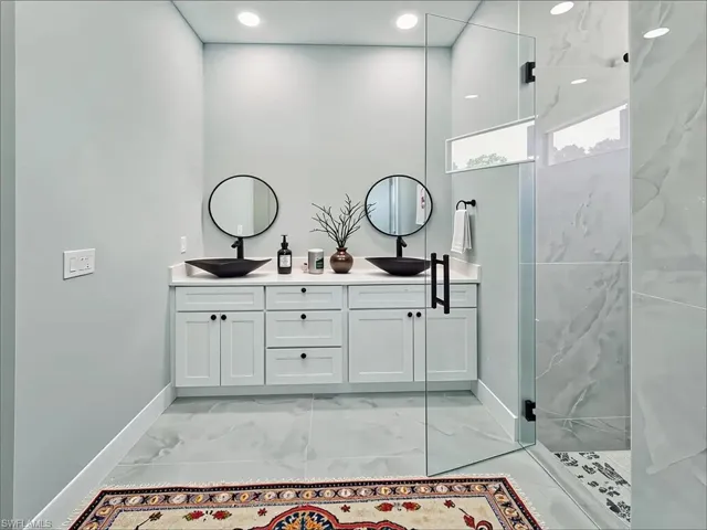 Full bath with marble look tiles, double vanity, and walk in shower