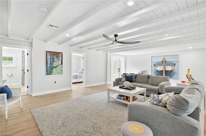 Living room with light wood finished floors, a ceiling fan, a wood ceiling with exposed beams, recessed lighting, and wooden walls