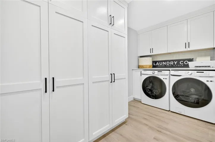 Laundry area featuring separate washer and dryer, cabinet space, and light wood-style floors
