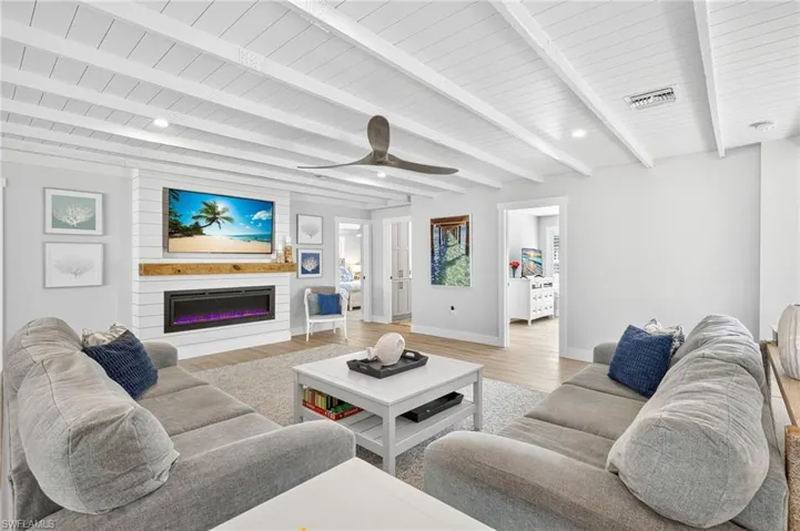 Living room with light wood-style flooring, a glass covered fireplace, a wood ceiling with exposed beams, and ceiling fan