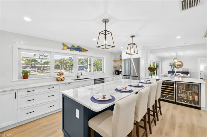 Kitchen featuring beverage cooler, light stone countertops, white cabinets, stainless steel appliances, and light wood-type flooring