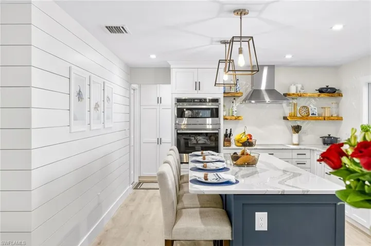 Kitchen featuring open shelves, light wood-style flooring, white cabinetry, wall chimney range hood, and double oven