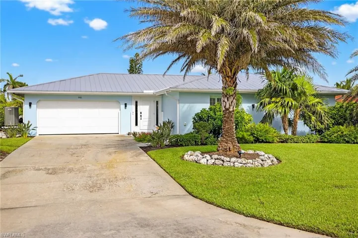 Ranch-style house featuring driveway, a front yard, stucco siding, a garage, and a metal roof