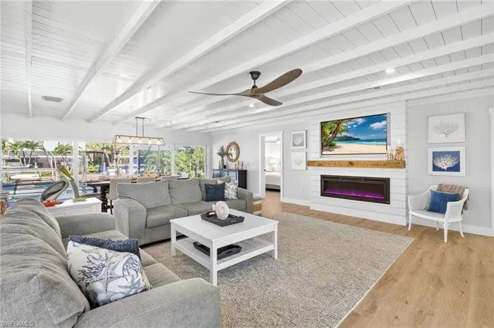 Living room with light wood-style flooring, a glass covered fireplace, a ceiling fan, and a wooden ceiling with exposed beams