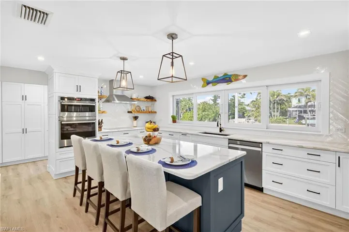 Kitchen featuring white cabinetry, a kitchen bar, light stone counters, appliances with stainless steel finishes, and hanging light fixtures