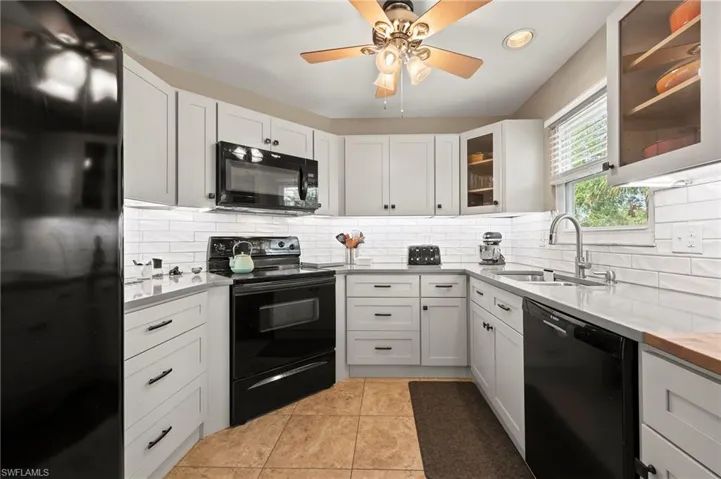 Kitchen with glass insert cabinets, light countertops, decorative backsplash, black appliances, and a sink
