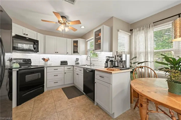 Breakfast nook and kitchen featuring black appliances, a ceiling fan, a sink, backsplash, and glass insert cabinets.