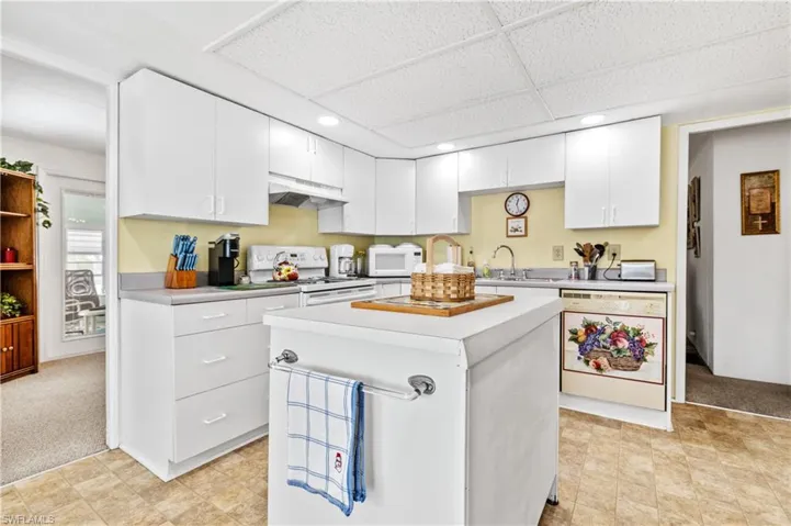 Kitchen featuring white cabinets, light countertops, light colored carpet, white appliances, and a paneled ceiling