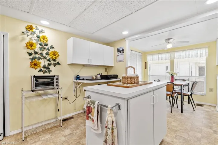 Kitchen with light countertops, white cabinets, a kitchen island, ceiling fan, and recessed lighting