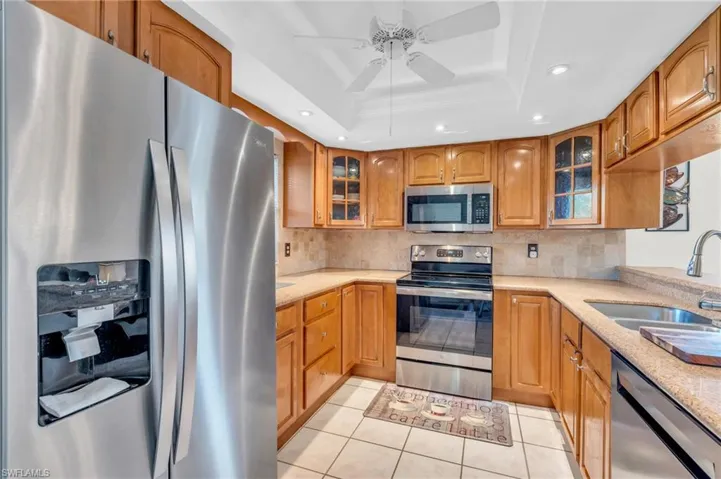 Kitchen with ceiling fan, sink, a tray ceiling with new stainless steel appliances, granite counters, ceiling fan, breakfast barappliances with stainless steel finishes