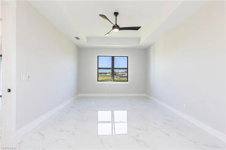 Spare room featuring light marble finish flooring, ceiling fan, and a tray ceiling