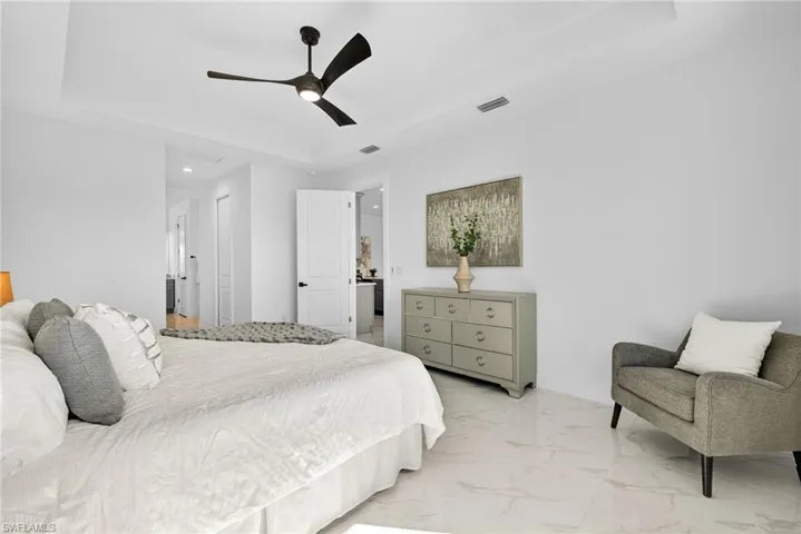 Bedroom featuring a tray ceiling, light marble finish flooring, and a ceiling fan