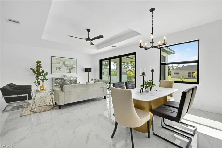 Dining space with ceiling fan, a chandelier, light marble finish floors, and a raised ceiling