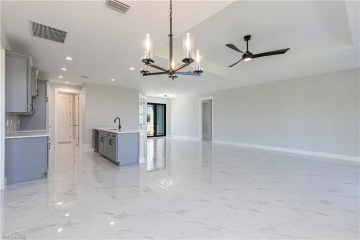 Kitchen with gray cabinets, suspended lighting, open floor plan, a kitchen island with sink, and a ceiling fan