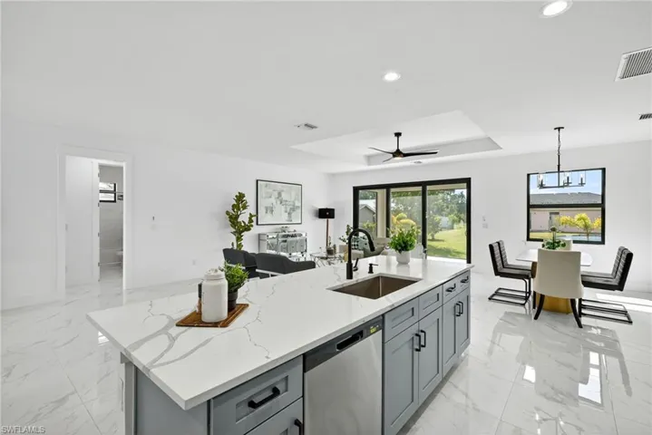 Kitchen with a tray ceiling, light stone counters, dishwasher, gray cabinets, and a ceiling fan