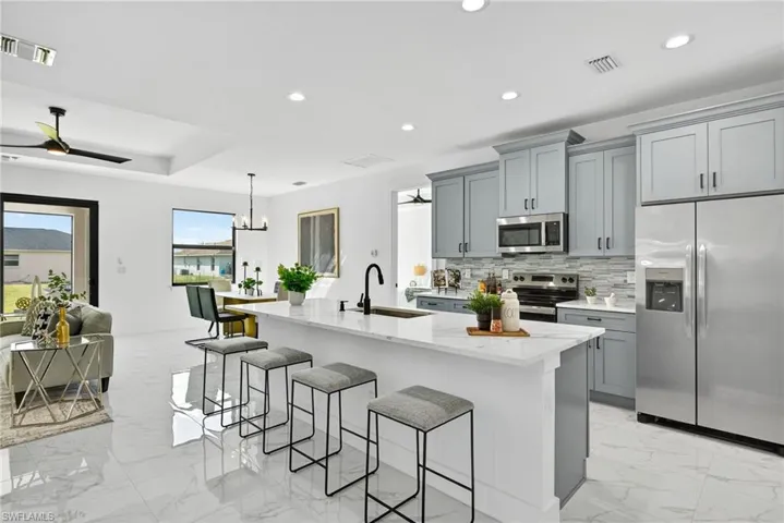 Kitchen featuring stainless steel appliances, a ceiling fan, a kitchen breakfast bar, light stone countertops, and gray cabinets