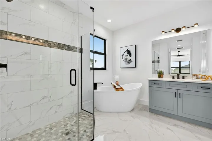 Full bath featuring light marble finish flooring, vanity, a marble finish shower, a freestanding bath, and recessed lighting