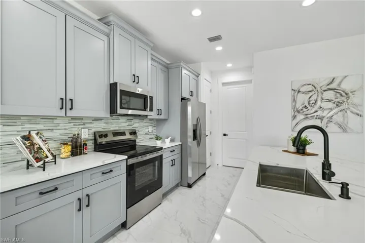 Kitchen with stainless steel appliances, gray cabinetry, light stone counters, light marble finish flooring, and recessed lighting