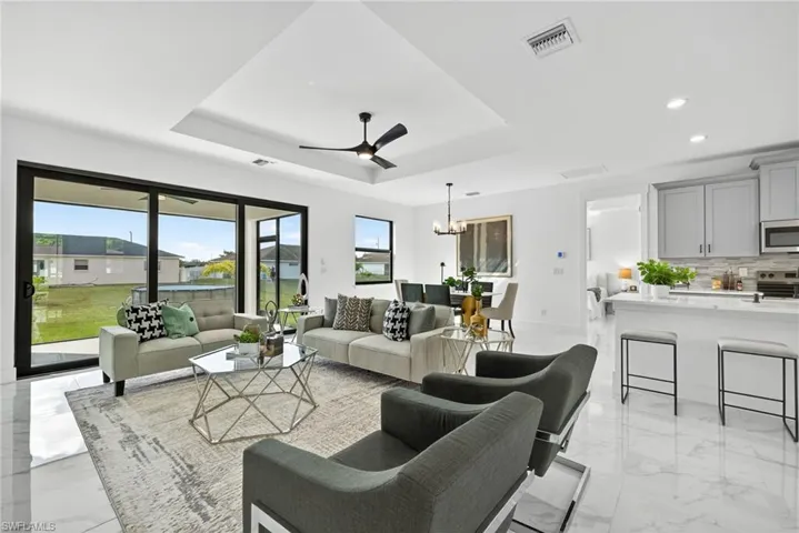 Living room featuring a raised ceiling, suspended lighting, a ceiling fan, and light marble finish flooring