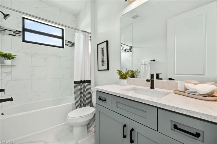 Full bathroom with vanity, shower / bath combo, and light marble finish flooring