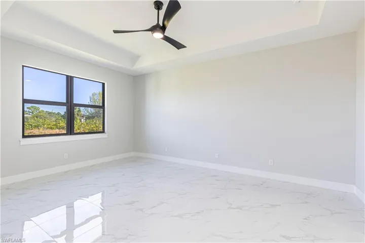 Spare room with a raised ceiling, a ceiling fan, and light marble finish flooring