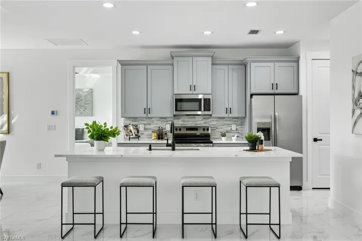 Kitchen with light stone counters, stainless steel appliances, gray cabinets, recessed lighting, and a kitchen breakfast bar