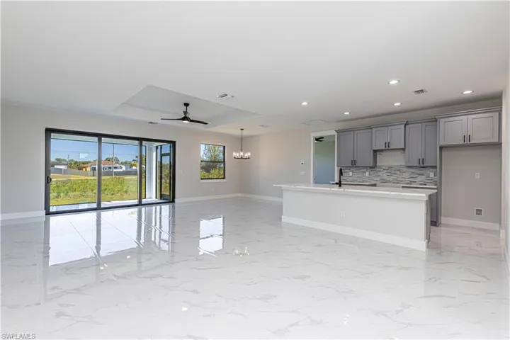 Kitchen featuring hanging lights, gray cabinets, open floor plan, a center island with sink, and a raised ceiling