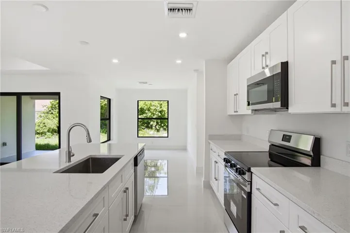 Modern kitchen featuring white shaker cabinetry, stainless steel appliances, light-toned countertops, a kitchen island with an undermount sink, and recessed lighting