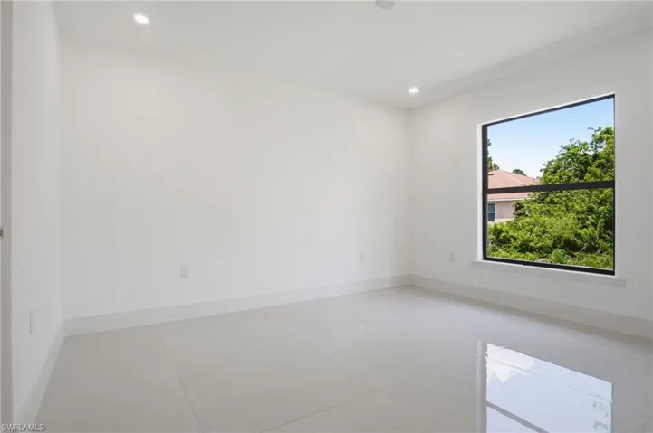 Spacious room featuring neutral paint, large format tile flooring, recessed lighting, and a prominent window with dark framing