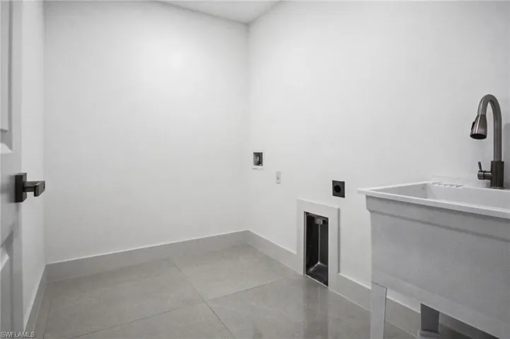 Dedicated laundry room featuring light gray floor tiles, a utility sink with a gooseneck faucet, and white baseboards