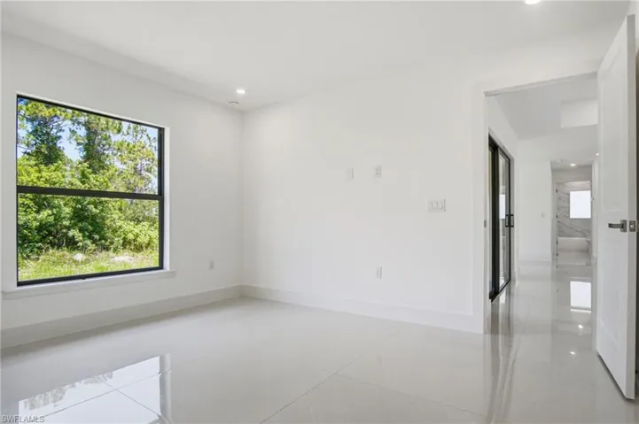 Bright interior space with a large window, white walls, recessed lighting, and glossy tile flooring