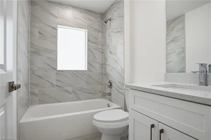 Bathroom featuring a white tub, shower with large format tile surround, vanity with stone countertop, and an integrated rectangular sink