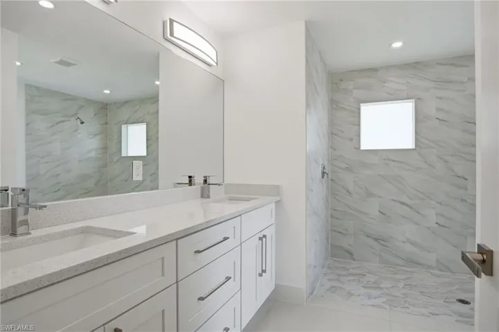 Contemporary bathroom featuring a dual vanity with white shaker cabinetry, light speckled countertops, and brushed nickel hardware