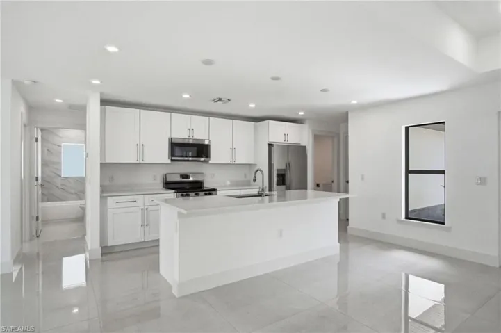 Bright kitchen featuring white cabinetry, stainless steel appliances, a center island with sink, and recessed lighting
