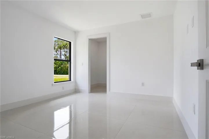 Bright interior space featuring large format light-toned tile flooring, clean white walls, and a window with black trim