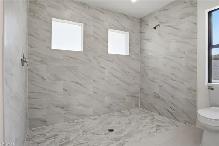 Walk-in shower featuring large format marbled tile walls, mosaic tile flooring, a chrome showerhead, and two frosted windows