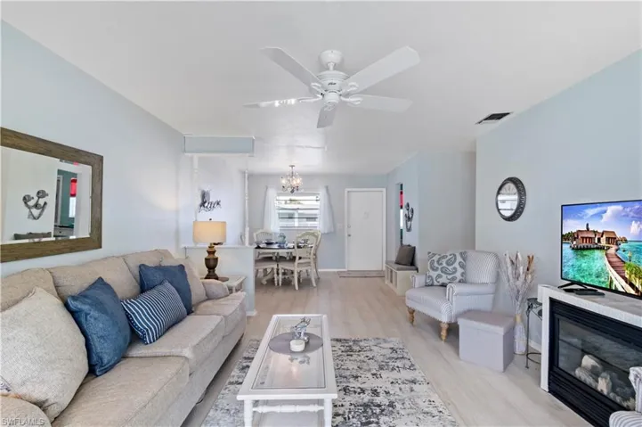 Living room with ceiling fan with notable chandelier and light hardwood / wood-style flooring
