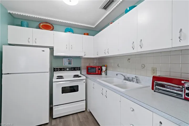 Kitchen featuring white appliances, wood-type flooring, sink, and white cabinets
