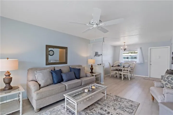 Living room with light wood-type flooring and ceiling fan with notable chandelier