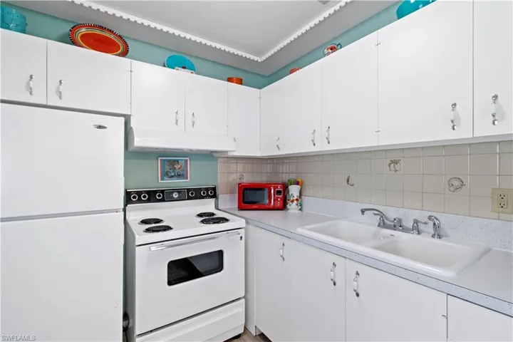 Kitchen featuring backsplash, sink, white appliances, and white cabinetry