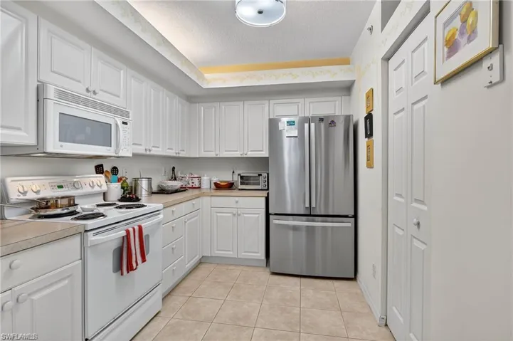Kitchen featuring white appliances, light countertops, white cabinets, light tile patterned floors, and a textured ceiling