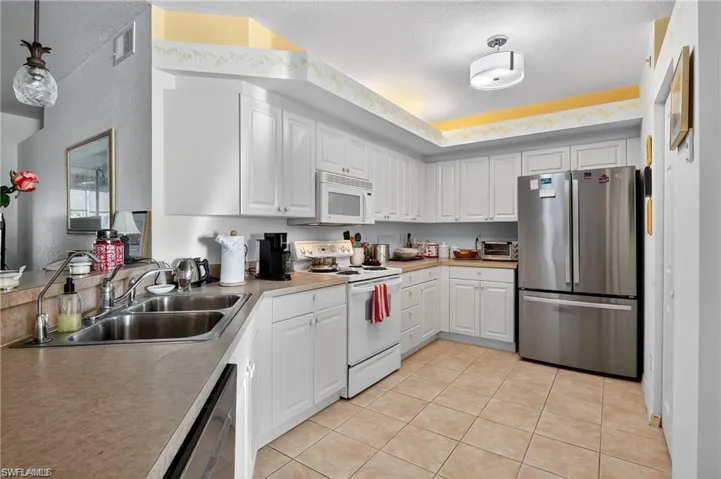 Kitchen with white cabinetry, appliances with stainless steel finishes, a textured ceiling, light tile patterned floors, and light countertops