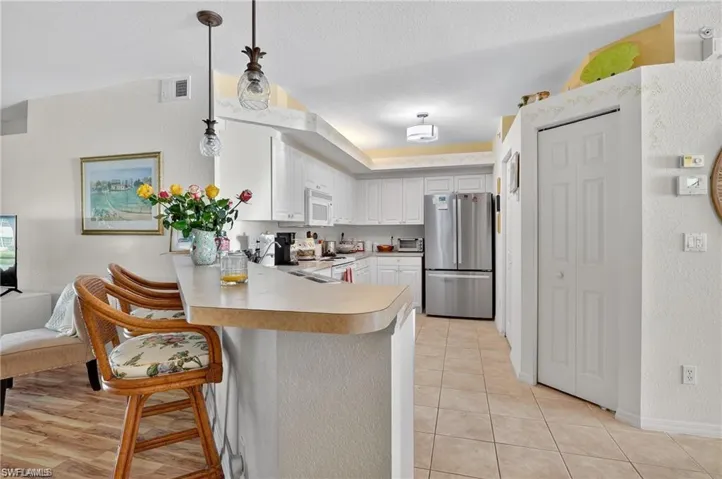 Kitchen with light countertops, a peninsula, a kitchen breakfast bar, pendant lighting, and white appliances