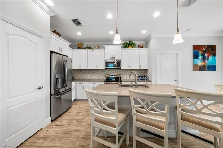 Spacious kitchen featuring an island with pendant lighting, stainless steel appliances, white cabinetry with crown molding, a mosaic tile backsplash, and wood-finish flooring