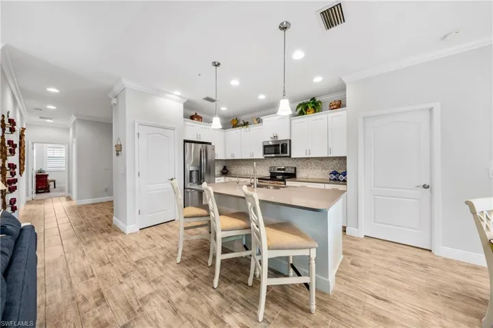 Modern kitchen featuring white cabinetry, stainless steel appliances, a light-toned countertop, mosaic tile backsplash, and wood-finish flooring