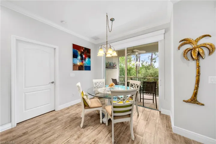 Dining area featuring wood-finish flooring, a contemporary chandelier, crown molding, and a sliding glass door leading to an outdoor balcony