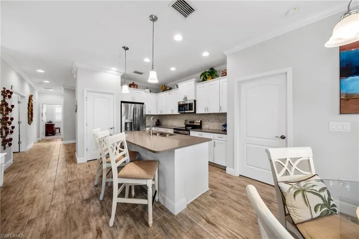 Kitchen featuring wood-finish flooring, white cabinetry, a neutral-toned countertop island, stainless steel appliances, and recessed lighting